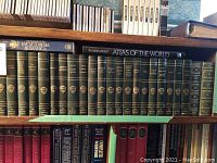Shelf with several dark green hardcover volumes of The Harvard Classics series in deluxe edition, along with blue hardcover Encyclopedia Britannica volume and Reader's Digest Atlas of the World.