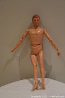 Nude articulated G.I. Joe figure standing on white cloth against neutral wall