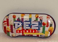 Image shows metal PEZ eyeglass case with colorful dispenser character graphics and PEZ logo on lid