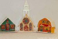 Nine vintage Christmas tree light covers including eight houses and one church arranged in a row