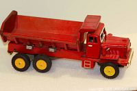 Side angle of red metal dump truck showing details of tilt bed, ladder, and wheels.