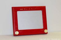 Front view of the red Etch A Sketch vintage toy with white knobs and clear screen area.