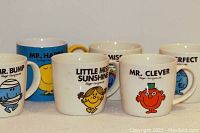 Group photo of six Mr. Men and Little Miss character mugs arranged in two rows. Front row includes Mr. Bump, Little Miss Sunshine, Mr. Clever. Back row includes Mr. Happy, Little Miss Giggles, Mr. Perfect.