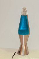 Lava lamp front view showing blue liquid, silver base and cap, cord visible, lamp off on a white background