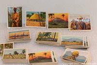 Stacks and fanned spread of vintage cigarette cards showing African scenes with people, huts, and landscapes.