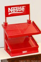 Full view of the red metal Nestlé point of sale display showing two angled product trays and prominent Nestlé signage on top and front.