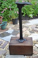 Full view of antique cobbler shoe stand featuring a metal shoe form mounted on a wooden base in an outdoor setting.