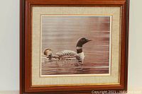 Front view of a framed print showing two loons swimming in water, with artist signature visible.