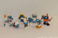 Photo of a group of eight vintage Smurfs figurines from the 1970s and 1980s, each painted blue with white hats and various accessories representing different characters.