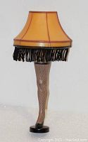 Front view of leg lamp night light with amber lampshade and black fringe; fishnet stocking leg standing on black base.