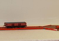 Close-up of red tin train boxcar on a section of red metal track with textured gray ends and turnouts.