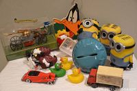 Photo of various toys arranged on a table showing minions, rubber ducks, toy vehicles, and a coin bank.