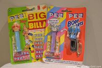 Photo showing two PEZ dispensers in original packaging, one Asterix character with a green background and one Police Officer character with an orange background.