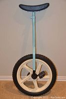 Full view of the blue unicycle showing the padded saddle, light blue metal frame, and white plastic rim with black tire and pedals.