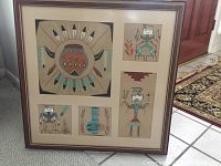 Photo showing all five framed Navajo sand paintings arranged in a single frame with beige matting and dark frame. Variations in Navajo sand painting designs visible.