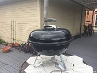 Photo of the closed 22-inch black Weber charcoal grill on metal legs, sitting on an outdoor table, showing the lid and handle.