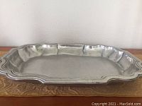 Front view of large rectangular pewter tray on a wooden surface showing overall shape and condition.