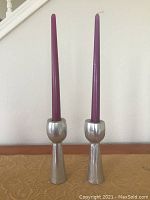 Front view of two pewter candle sticks each holding a tall purple tapered candle, showing size and design.