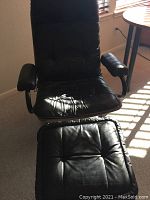 Black leather recliner chair with tufted cushioned seat and backrest, and armrests, photographed from front in natural light.