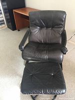 Front view of black leather armchair with matching ottoman on carpet