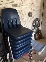 Stack of 7 blue plastic and metal school chairs stacked against a wall.