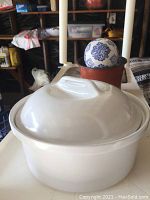 White ceramic casserole dish with lid on, resting on a surface with other items visible in background