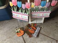 Photo shows four decorative metal yard signs: two Easter themed signs each with colorful tulips and Happy Easter text, one round pumpkin shape with Welcome message and frog detail, and one turkey shape with Welcome message and feather detail. All mounted on metal stakes for yard placement.