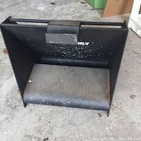 Black steel bullet trap angled with backstop plate, showing signs of use and rust, placed on concrete floor.