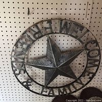 Front view of the round metal welcome sign mounted on a pegboard wall, showing the star and surrounding text.