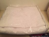 Photo of folded white duvet cover in plastic packaging on a flat surface.