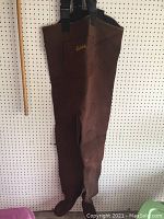 Full view of dark brown insulated waders hanging showing adjustable straps and foot coverage.