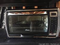 Front view of Oster convection toaster oven showing glass door, brand logo, and digital control panel.