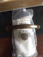 Photo of one antique bronze drawer pull lying on packaging with label 'Top Knobs' and 'Pull 3-3/4 CC in German Bronze'.