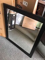 Black wood framed mirror displayed on carpet with cardboard box behind.