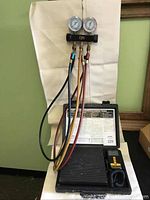 Full view of the CPS scale and gauge set in its open black carrying case with hoses hanging down, showing intended use setup.
