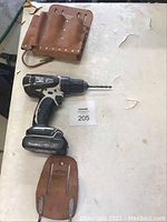 Makita 18V cordless drill with battery and two leather tool holders on a white surface.