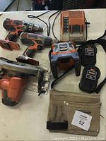 Lot showing two Ridgid cordless drills, a circular saw, two batteries, charger, radio, and tool belt on a table.