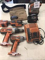 Overview of the lot showing four orange Ridgid cordless power tools, cordless radio, battery charger, battery, and tool belt.