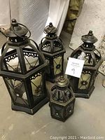 Four hexagonal metal decorative lanterns of varying sizes placed on floor, showing overall lot condition.