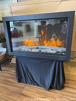 Front view showing fireplace insert powered on with flame effect, logs and black metal frame