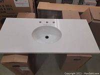White quartz vanity top resting on boxes showing oval undermount sink, faucet holes and polished edges