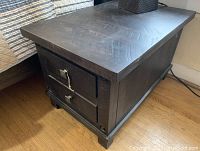Angled front-left view of charcoal-finished end table showing two drawers, tabletop, and base.