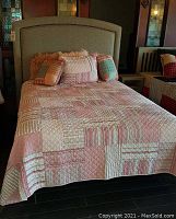 Taupe upholstered headboard on display with decorative nailhead trim visible around edge.