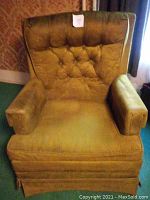 Front view of a vintage upholstered easy chair showing mustard yellow or olive green fabric with button tufted backrest and padded armrests.