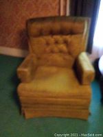 Full front view of a vintage mustard-yellow upholstered easy chair with tufted backrest, padded armrests, and skirted base.