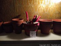 Photo showing 5 clay flower pots of varying sizes and several red-handled gardening tools in a small wooden basket.