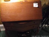 Closed view of wooden secretary desk with drop leaf front and curved drawer fronts below, showing wood grain and a lock on the front panel.