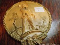 Photo of a circular ceramic wall decor showing a person in traditional attire on a bridge with trees in the background and a twisted rope style border