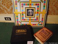 Bible Challenge board game upright showing colorful pattern and Earth image, with black box and 1001 Bible Questions and Answers book in front on carpet.