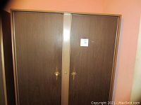 Closed metal clothing cabinet showing two doors with star-shaped handles. One handle is missing on right door.